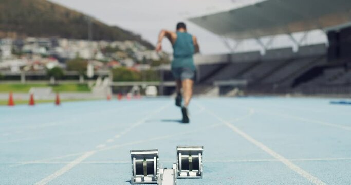 Athlete in starting position for a race on a sports track in a stadium. Rearview of an active man with feet on angled pedals. Runner sprinting fast in a lane while training for an olympic competition