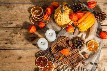 Autumn cozy composition. Scarf, warm mittens, candles, pumpkins, fall decor. Wooden background
