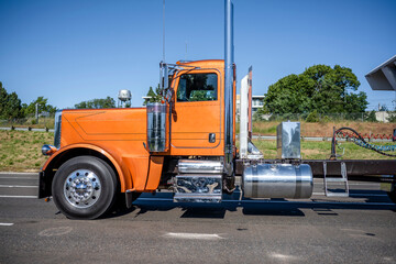 Stylish orange day cab classic big rig semi truck tractor with chrome accessories and tall exhaust...