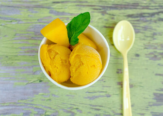 Frozen mango fruit sorbet, ice cream in a cup with a spoon on a rustic wooden background