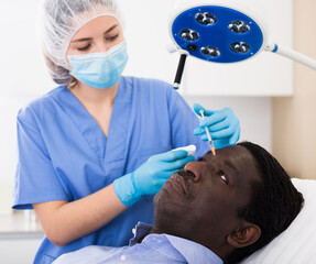 Afro american man getting procedure of injection for face skin tightening in aesthetic clinic