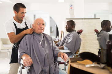 Professional stylist preparing aged man for haircutting, dressing hairdressing cape..