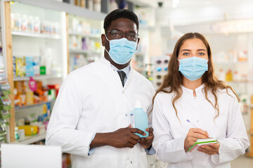 Portrait of two multinational pharmacists in protective masks, standing in the sales hall of a...