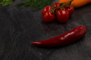 Close-up of a red hot chili pepper on a dark metal background with vegetables in the background.