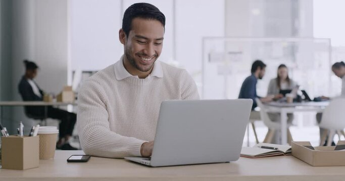 Happy business man checking his phone while working on a laptop in the office. Young corporate professional smiling after receiving good news via text message while sitting at his desk at work