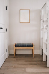 Bench beneath blank framed wall art in a light, neutral bedroom