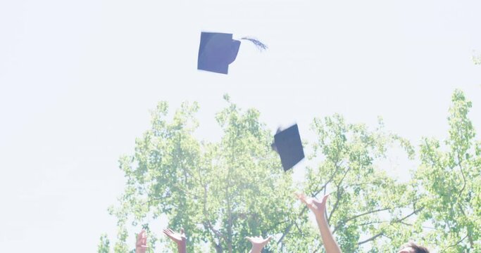 Group of graduates celebrating and throwing caps or hats into the air in tradition after university campus graduation ceremony. Smiling diverse men, women, friends graduating from college together