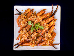 Crispy prawns in tamarind sauce in  white square dish, sprinkle with glaze and top with fried shallots and coriander. It has perfect balance of crispy, spicy, and sweet flavors.