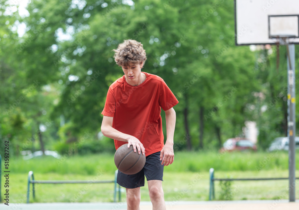 Wall mural teenager running in the stadium. cute young teenager in red t shirt with a ball plays basketball on 