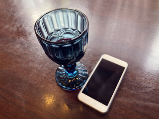 A glass of blue glass with the remains of wine and a white phone on the cafe table. The end of a...