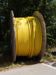 Eine große, mannshohe Kabeltrommel aus Holz. Aufgewickelt ist ein armdickes Kunststoff-Kabel. Es...
