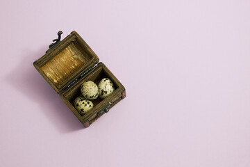 Colorful quail eggs in a wooden chest on a lilac background