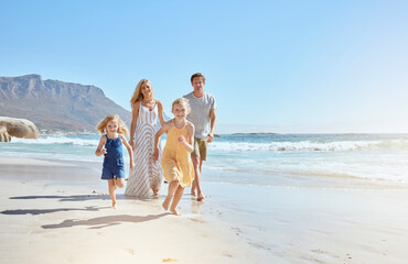 Joyful young family with two children running on the beach and enjoying summer vacation. Two energetic little girls running ahead while their mother and father follow in the background
