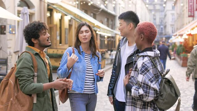 Mixed-race male and female friends standing in town and speaking together. Multi-ethnic group of young people having conversation outdoor standing at decorated street. Leisure, best friends concept