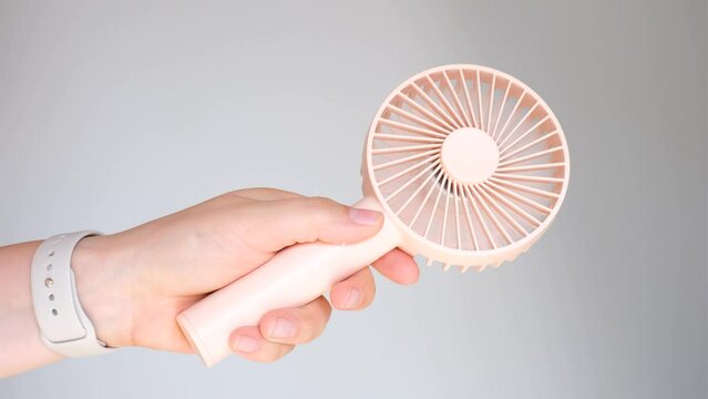Hand holding a pink mini fan on gray background close-up.