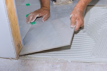 Placing ceramic floor tiles on adhesive surface with home bathroom construction working
