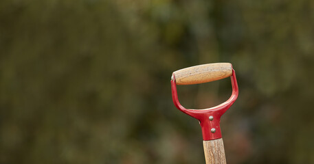 Closeup of a shovel handle in a garden outside against a blur background. Red gardening tool or equipment ready to be used in a backyard for shoveling, planting and basic outdoor maintenance