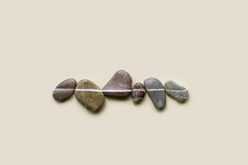 Obraz na płótnie Canvas Aesthetic minimal flat lay sea pebble stones with white line, beige background. Composition from natural colored stone on the same level. Balance or harmony concept, horizontal row rocks.