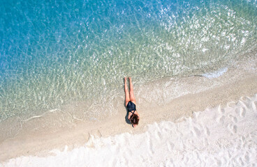 Aerial view, women lounging, sunbathing on the beach and beautiful blue water waves on the island...