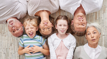 A family bonding together and being playful, showing different expressions while bonding and enjoying quality time. Above happy fun family making silly faces lying together on a living floor at home. - obrazy, fototapety, plakaty