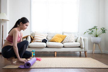 Asian young woman with exercise mat preparing for sports training. Fitness lesson and gathering the carpet from the floor