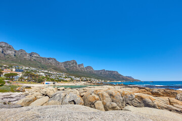 Landscape of a summer holiday destination with a unique mountain range near a rocky beach in South Africa. View of the twelve apostles in Cape Town and a calm ocean against a bright blue horizon.
