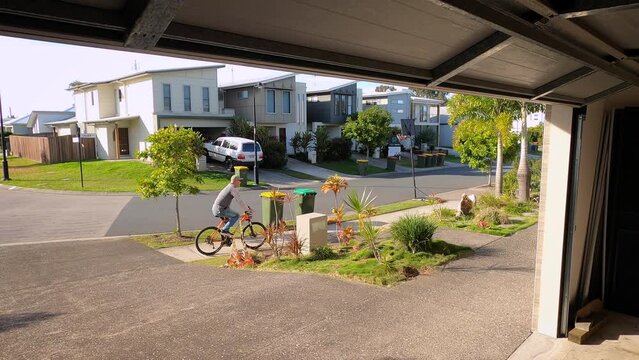 As the garage door goes up, a man rides his bike down a driveway and onto a suburban footpath and forgets to lock up.