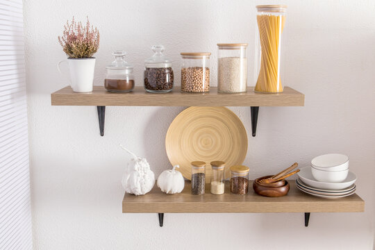 open wooden shelves with various glass jars with a wooden lid filled with spices, coffee, spaghetti. stylish decor in the modern kitchen. front view.
