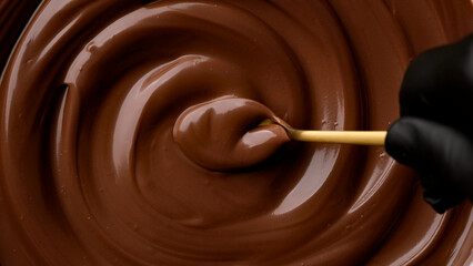 Hand stirring melted dark chocolate with golden spoon, close up. Liquid hot chocolate. Confectioner...