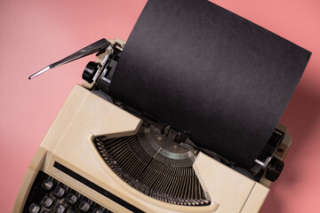 Typewriter with black paper on a pink background, vintage concept.