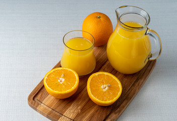 Glass and jug with orange juice on a wooden stand, sliced orange, background line
