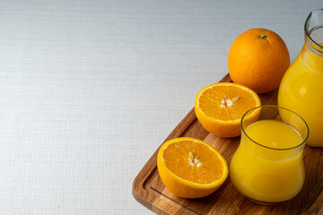 Glass and jug with orange juice on a wooden stand, sliced orange, background line
