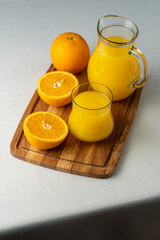Glass and jug with orange juice on a wooden stand, sliced orange, background line
