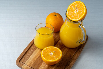 Glass and jug with orange juice on a wooden stand, sliced orange, background line
