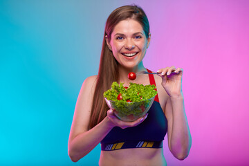 Sporty woman in sportswear green salad in glass bowl and red tomato on fork. Female fitness portrait isolated on neon multicolor background.