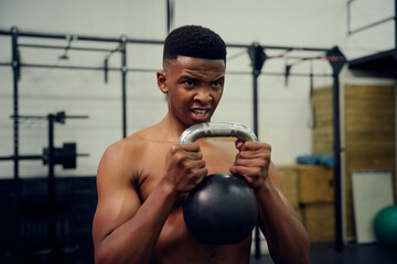 African American male doing cross fit in gym. Mixed race male using a kettlebell during exercise. High quality photo