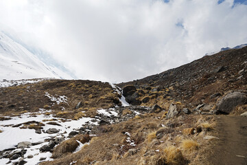 Rocky trail pathway with natural landscape view of snowcapped mountain range with cloudy blue sky- Himalayas ridge, Nepal