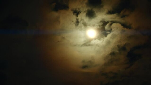 Timelapse of full moon, dark dramatic clouds in night sky, anamorphic time lapse