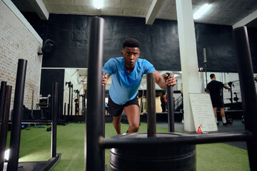 African American male working out intensely during cross fit training. Male athlete pushing the sled in the gym. High quality photo