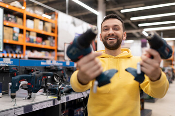 satisfied customer in a hardware store holding two cordless screwdrivers with a big smile on his face