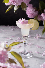 Spring still life with a glass of cold Margarita with lime, pink sakura flowers 