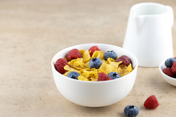 Delicious golden corn flakes in a bowl with berries, milk on a beige background. Side view, copy space. Healthy breakfast with corn flakes and milk.