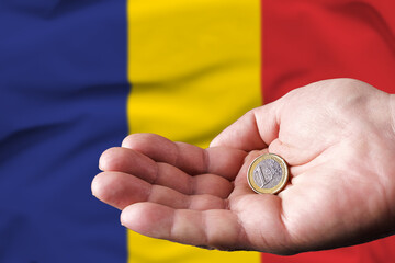 Coin one euro in the hand of a man, the flag of Romania on the background