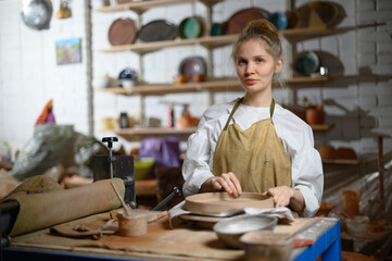 Obraz na płótnie Canvas A ceramist makes a plate. Woman in an apron works in a pottery workshop. 