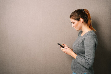 Young woman looking at her cell phone, brown wall with copy space