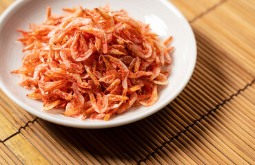 Dried sakura shrimps on a plate placed on a bamboo luncheon mat.