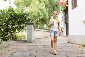 Schoolgirl back to school after summer vacations. Happy Child smiling early morning outdoor. 