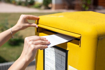 Hand throws white letter into yellow mailbox