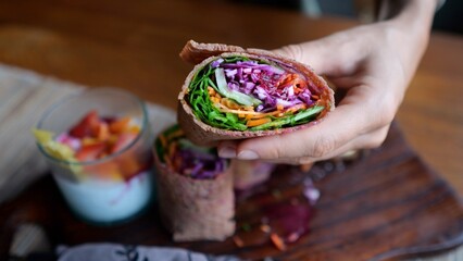 Appetizing vegetarian rolls wrapped in flatbread filled with various vegetables. On a wooden plate, a healthy breakfast of a vegetable dish and a drink with fruits and berries. Delicious vegan.