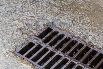 Rainwater running down to storm drain with cast iron grid